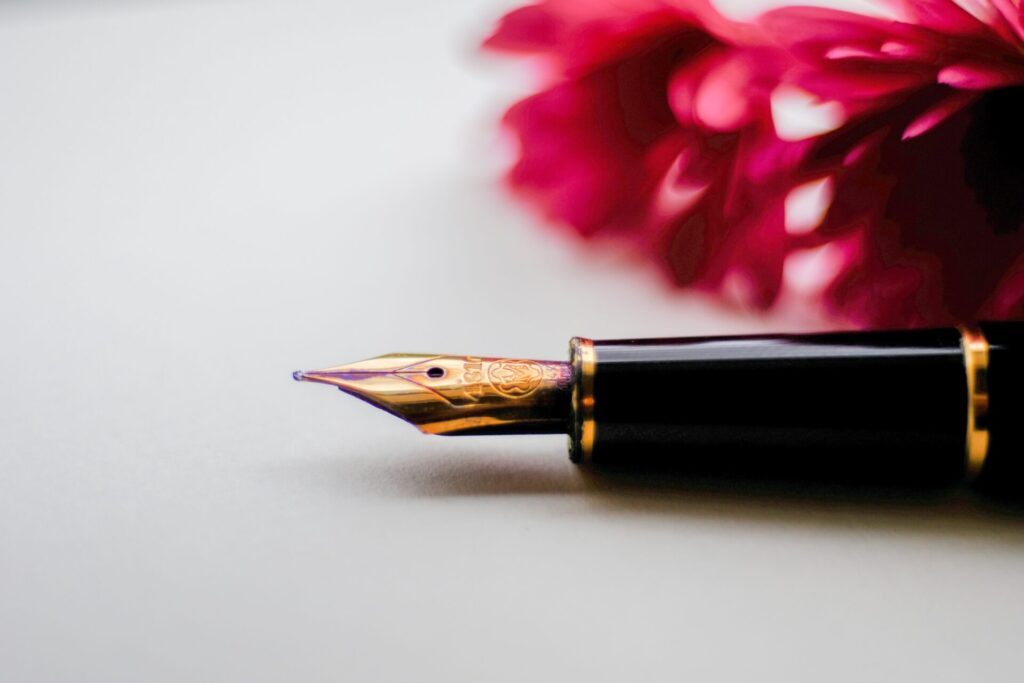 A fountain pen tip with a pink flower in the background.